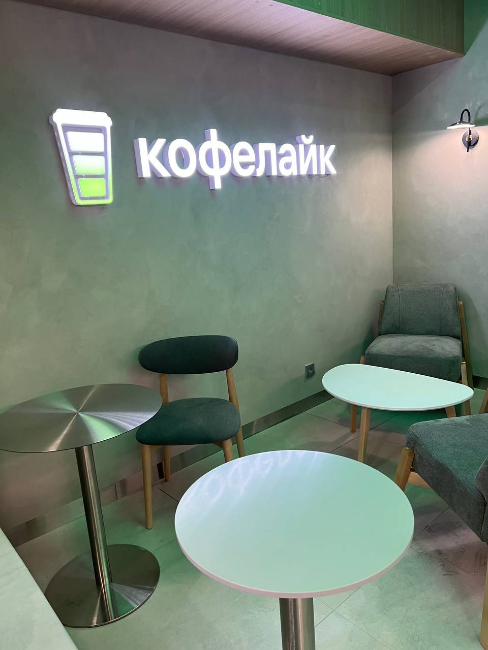 Зона посадки в кофейне: столики, стулья и световой логотип